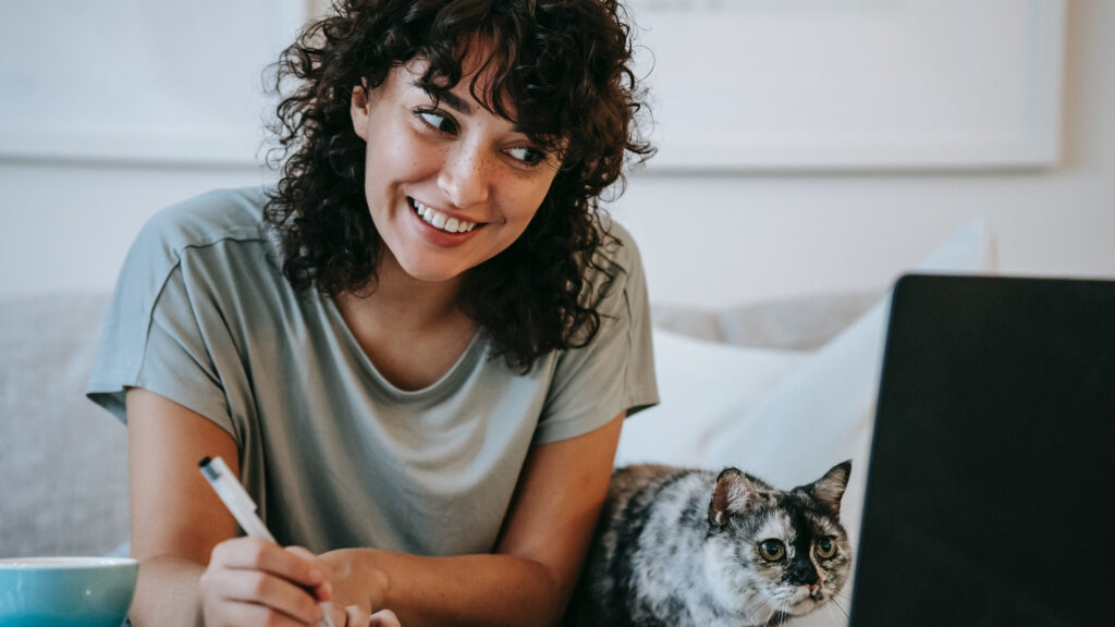 Content marketing person with cat writing in planner while using laptop